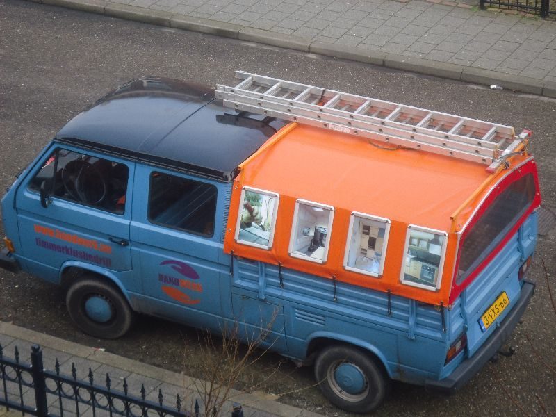 De blauw-oranje Handwerk-bus met ladders op het dak